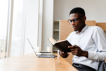 Poster - Afro american focused man reading book while working with laptop