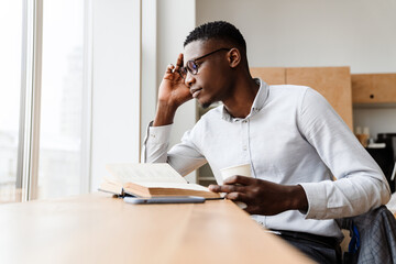 Poster - Afro american focused man reading book and drinking coffee