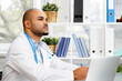 © fotofabrika - Mixed race male doctor sitting at his working table in hospital