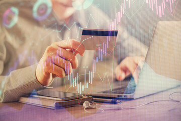 Double exposure of man hands holding a credit card and Forex graph drawing. Stock trading and digital fintech in Internet E-commerce concept.