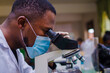 © Vic Josh - young handsome african scientist in the lab carefully carrying out experiments while using a microscope