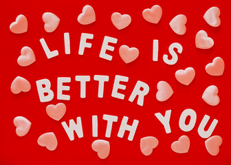 Valentine's Day red background with pink hearts and phrase Life Is Better With You lined with white wooden letters.Mother's Day, March 8 greeting card