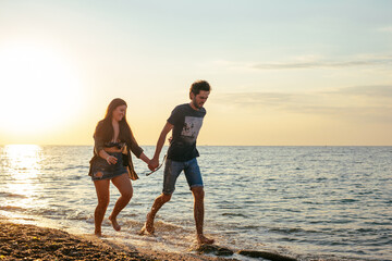 Wall Mural - young caucasian couple walking on beach with siberian husky dogs during beautiful sunset or sunrise. Playing with dogs. Pets are the members of family concept