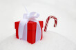 Red gift box with white bow and candy cane on the snow. Romantic present for Christmas or New Year holiday