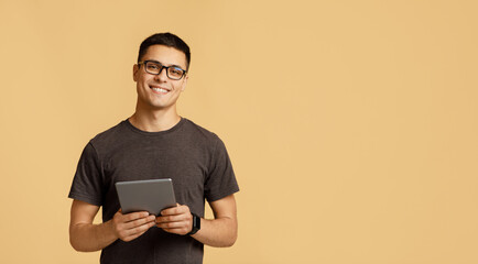 cheerful young attractive man in glasses looks at camera, holds digital tablet on online lesson