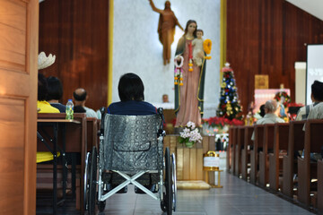 Wall Mural - Rear view of people sitting on wheelchair in church for pray to jesus and virgin mary statue.