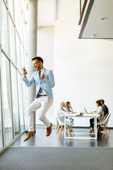 Wall Mural - Young businessman with smartphone in a modern office jumping after receving a great news