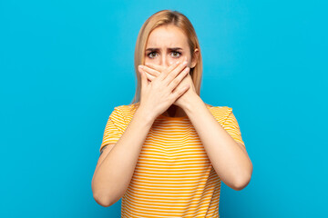 young blonde woman covering mouth with hands with a shocked, surprised expression, keeping a secret or saying oops