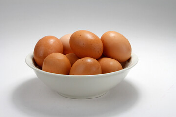 Group of brown eggs in a white bowl on a neutral background close up