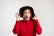 Surprised stylish woman. Trend look. Hipster model. Beautiful coquettish lady in red sweater holding flaps black hat posing at camera isolated on white.