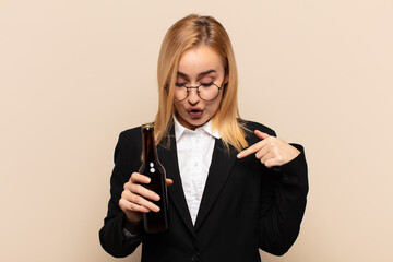 Wall Mural - young blonde woman feeling shocked, open-mouthed and amazed, looking and pointing downwards in disbelief and surprise