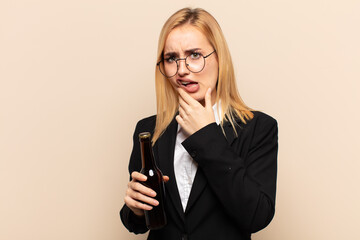 Wall Mural - young blonde woman with mouth and eyes wide open and hand on chin, feeling unpleasantly shocked, saying what or wow