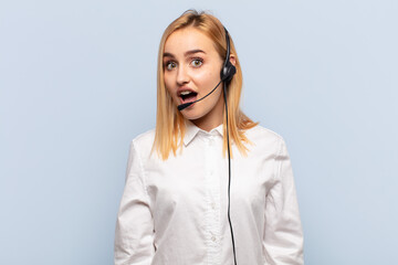 Wall Mural - young blonde woman looking very shocked or surprised, staring with open mouth saying wow