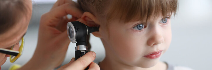 Otorhinolaryngologist examines little girl's ear with otoscope. Adenoiditis as cause of otitis media in children concept.