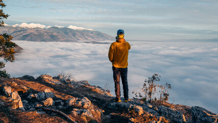 Wall Mural - Adventurous man hiker on top of a steep rocky cliff overlooking winter alpine like moutains landscape. Concept: Adventure, Explore, Hike, Lifestyle. Composite.