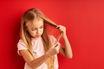 Wall Mural - child girl examining her hair ends with sadness, check the split ends, want to cut, isolated on red background