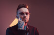 © Fxquadro - Serious and tattooed hipster businessperson with beard and stylish haircut poses in dark room with lights and colourful walls touching his face with finger.