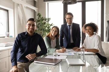 Group portrait of smiling successful multiracial businesspeople pose in modern office at team briefing together. Happy motivated millennial diverse multiethnic employees colleagues show unity.