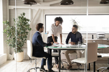 Wall Mural - Diverse colleagues coworkers gather in boardroom brainstorm discuss company business ideas together. Multiracial businesspeople talk consider corporate plans, engaged in team briefing meeting.