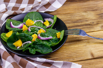 Tasty salad with spinach, orange, red onion and sesame seeds on wooden table. Healthy food or vegetarian concept