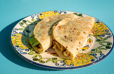 Wall Mural - Delicious traditional quesadillas with chicken and spinach inside, on a handmade plate on a blue table.