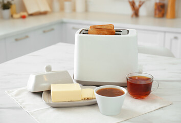 Canvas Print - Modern toaster with bread slices, jam and butter on white marble table in kitchen