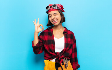 young latin woman feeling successful and satisfied, smiling with mouth wide open, making okay sign with hand