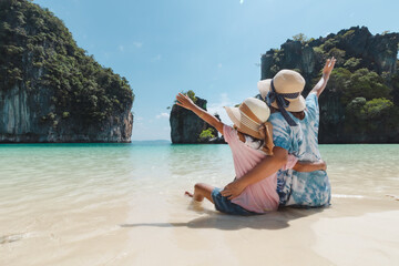 Asian mother and child girl sitting on the beach and enjoying with beautiful nature together in their vacation. Summer holidays and family travel concept. Travelling in Thailand.