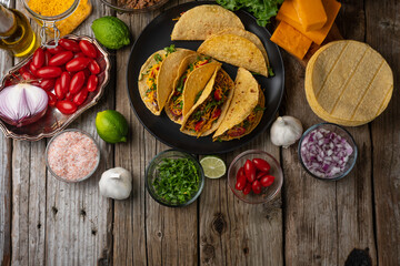 Wall Mural - Plate with delicious mexican tacos on rustic wooden table with ingredients for cooking background. Concept of traditional meal. Appetizing photo for menu or cookbook.
