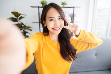 Pretty young asian female with big smile sitting at living room. She having fun taking light cheerful selfie on blurred background