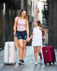 woman and a girl are walking the streets of a European city on vacation with suitcases