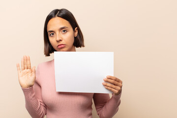 Canvas Print - young latin woman looking serious, stern, displeased and angry showing open palm making stop gesture