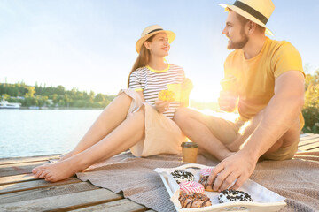 Sticker - Young couple eating sweet donuts and drinking coffee near river