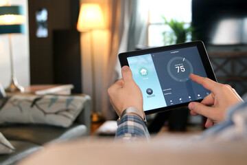 man is adjusting a temperature using a tablet with smart home app in modern living room
