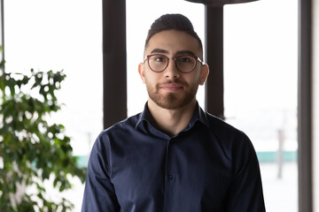 Headshot portrait of young Arabic male employee in glasses pose in office workplace. Profile picture of successful confident millennial arab businessman in spectacles show leadership and motivation.