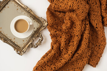Wall Mural - Lifestyle composition with cup of coffee with milk on vintage golden tray and knitted brown blanket plaid on white background. Retro styled concept.