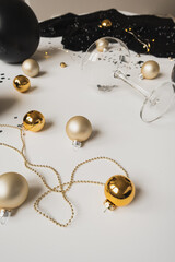 Wall Mural - Christmas / New Year celebration concept. Champagne glass, sparkling confetti, dress, baubles on table. Minimalistic holiday party composition. Black and gold colors.