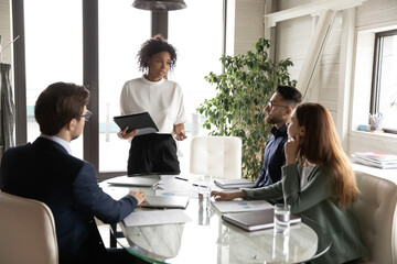 Canvas Print - Confident young African American businesswoman stand lead head meeting with multiracial colleagues in office. Successful biracial woman CEO brainstorm with diverse coworkers at team briefing.