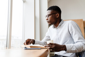 Poster - Afro american focused man reading book and drinking coffee