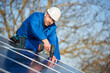© anatoliy_gleb - Male engineer in blue suit and protective helmet installing solar photovoltaic panel system using screwdriver. Professional electrician mounting module on roof. Alternative energy ecological concept.