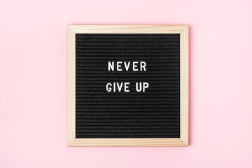 Wall Mural - Never give up. Motivational quote on black letter board on pink background. Concept inspirational quote of the day. Greeting card, postcard