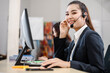Young Asian cheerful woman staff at service desk talking on phone in a call center with her colleague team working, female operator agent with headsets, customer service or technical support concept