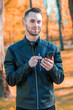 © InfinitumProdux - Youthful Satisfied Guy Using Black Smartphone at the Beautiful Autumn Park. Handsome Smiling Young Man with Mobile Phone at Sunny Day - Medium Shot Portrait