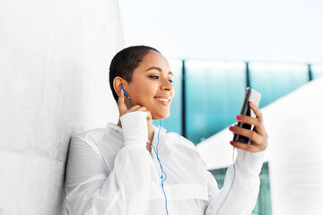 Sticker - fitness, sport and technology concept - happy smiling young african american woman with earphones listening to music on smartphone outdoors