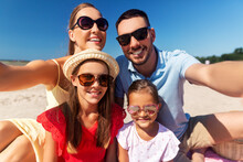 Family, Leisure And People Concept - Portrait Of Happy Mother, Father And Two Daughters In Sunglasses Taking Selfie On Summer Beach