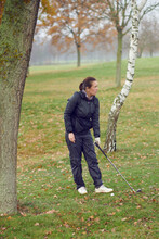 Woman Golfer Playing A Round Of Golf Standing Between Trees On A Cold Winter Day With Club In Hand Staring Out Over The Fairway