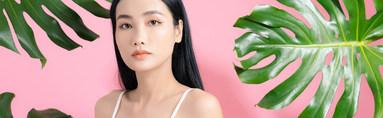 Wall Mural - Natural cosmetics. Sensual Asian woman against tropical leaves, looking at camera on pink background