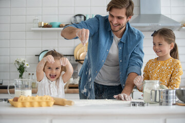 Wall Mural - smiling father and daughters baking in the kitchen and having fun