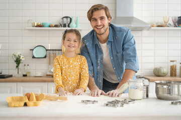 Joyful dad and daughter having fun while kneading dough on kitchen table, baking together