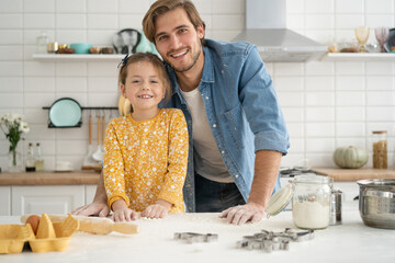 Wall Mural - Joyful dad and daughter having fun while kneading dough on kitchen table, baking together